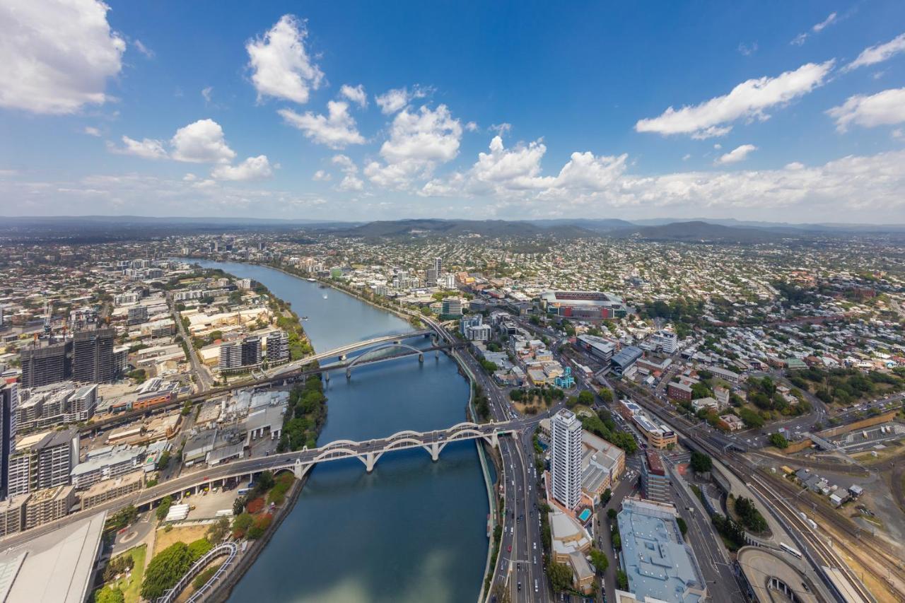 Meriton Suites Herschel Street, Brisbane Dış mekan fotoğraf The photo shows an aerial view of an urban landscape featuring a river winding through the city. There are several bridges crossing the river, which appears to be fairly wide. The surrounding area is densely populated with buildings, both residential