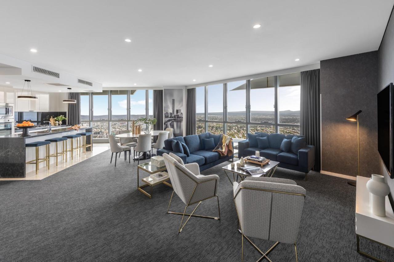 Meriton Suites Herschel Street, Brisbane Dış mekan fotoğraf The photo depicts a modern and stylish living area within a high-rise apartment. The space features large windows that offer a panoramic view of the cityscape. 

1. **Seating Area**: There are two blue sofas and several light-colored chairs arranged 
