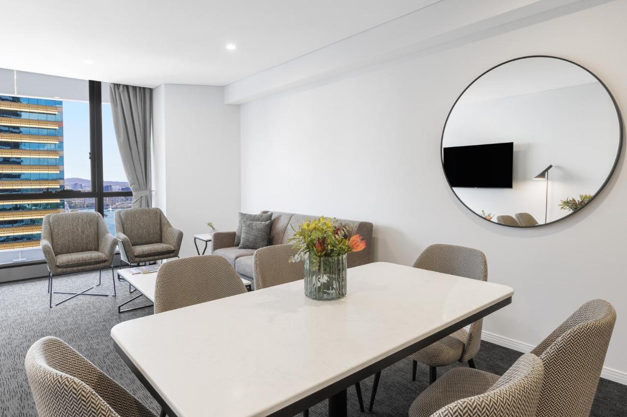 Meriton Suites Herschel Street, Brisbane Dış mekan fotoğraf The photo shows a modern and stylish living space. There is a cream-colored table with black accents at the center surrounded by upholstered chairs. A vase with flowers adds a touch of color to the table. In the background, there are two comfortable 