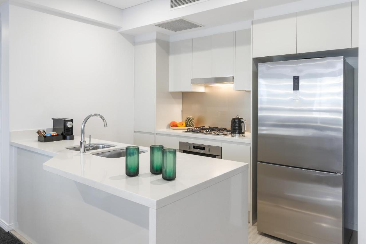 Meriton Suites Herschel Street, Brisbane Dış mekan fotoğraf The photo depicts a modern kitchen with a clean and minimalist design. The kitchen features a large island with a white countertop, accompanied by two green glass vases. 

To one side, there is a stainless steel refrigerator and a built-in oven and s